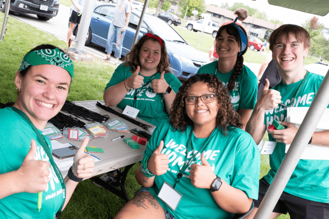 a group of UWGB students in green t-shirts smiling and giving a thumbs up as they welcome new freshmen for move-in